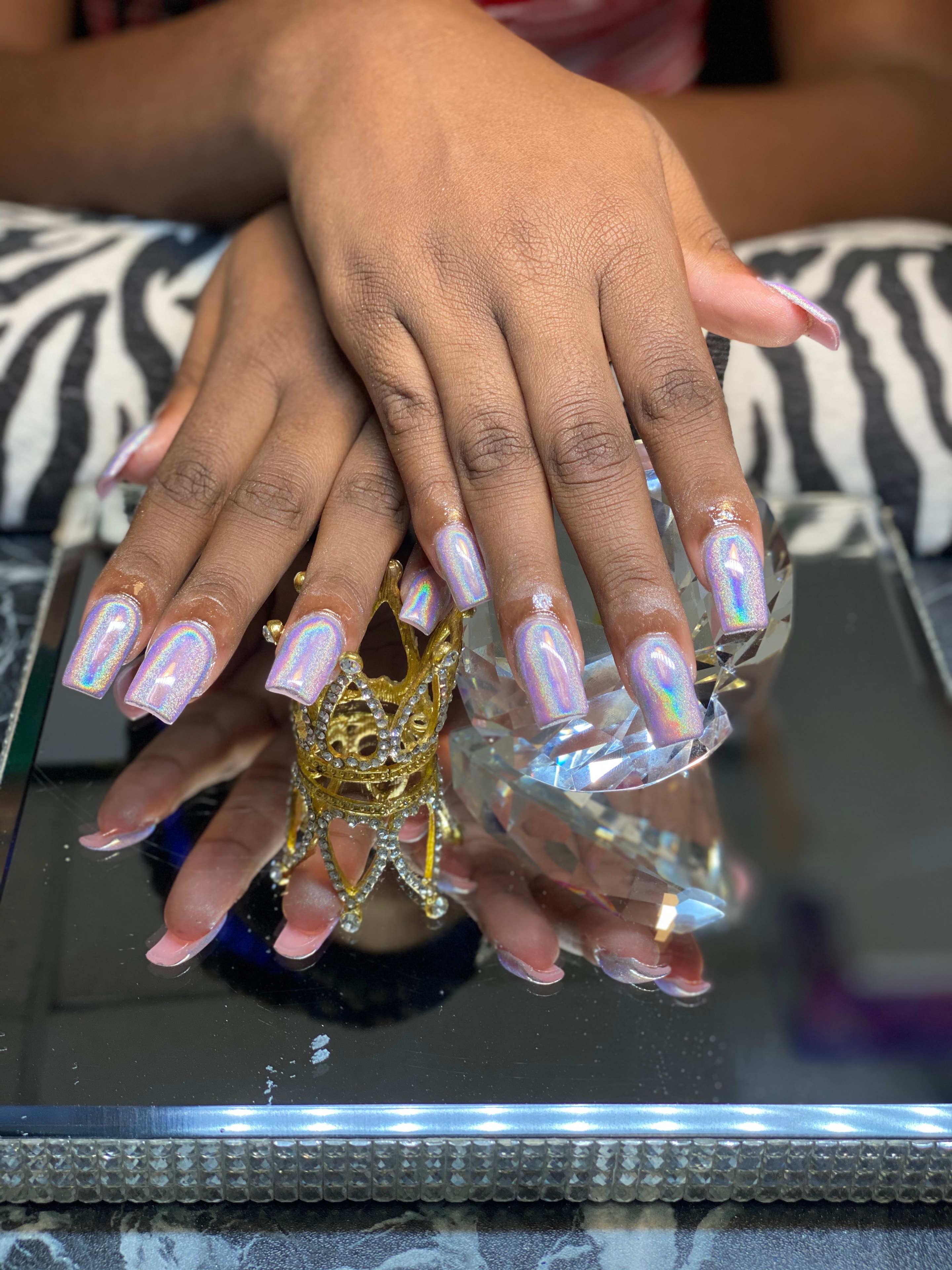 Holographic iridescent acrylic nailz on a mirrored surface with a jeweled crown