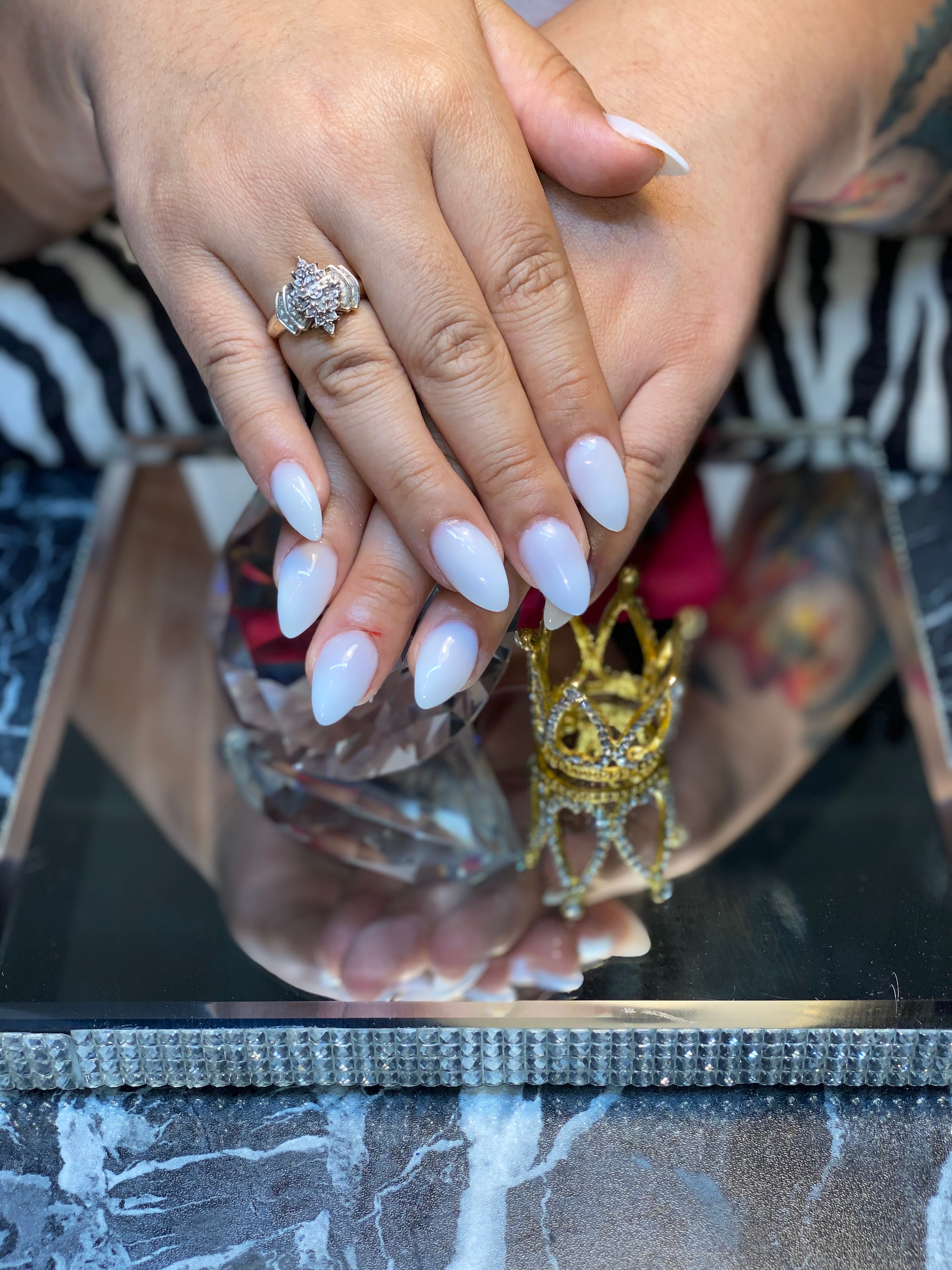 Milky white almond nailz with a gold ring, styled on a mirrored tray with a gold crown