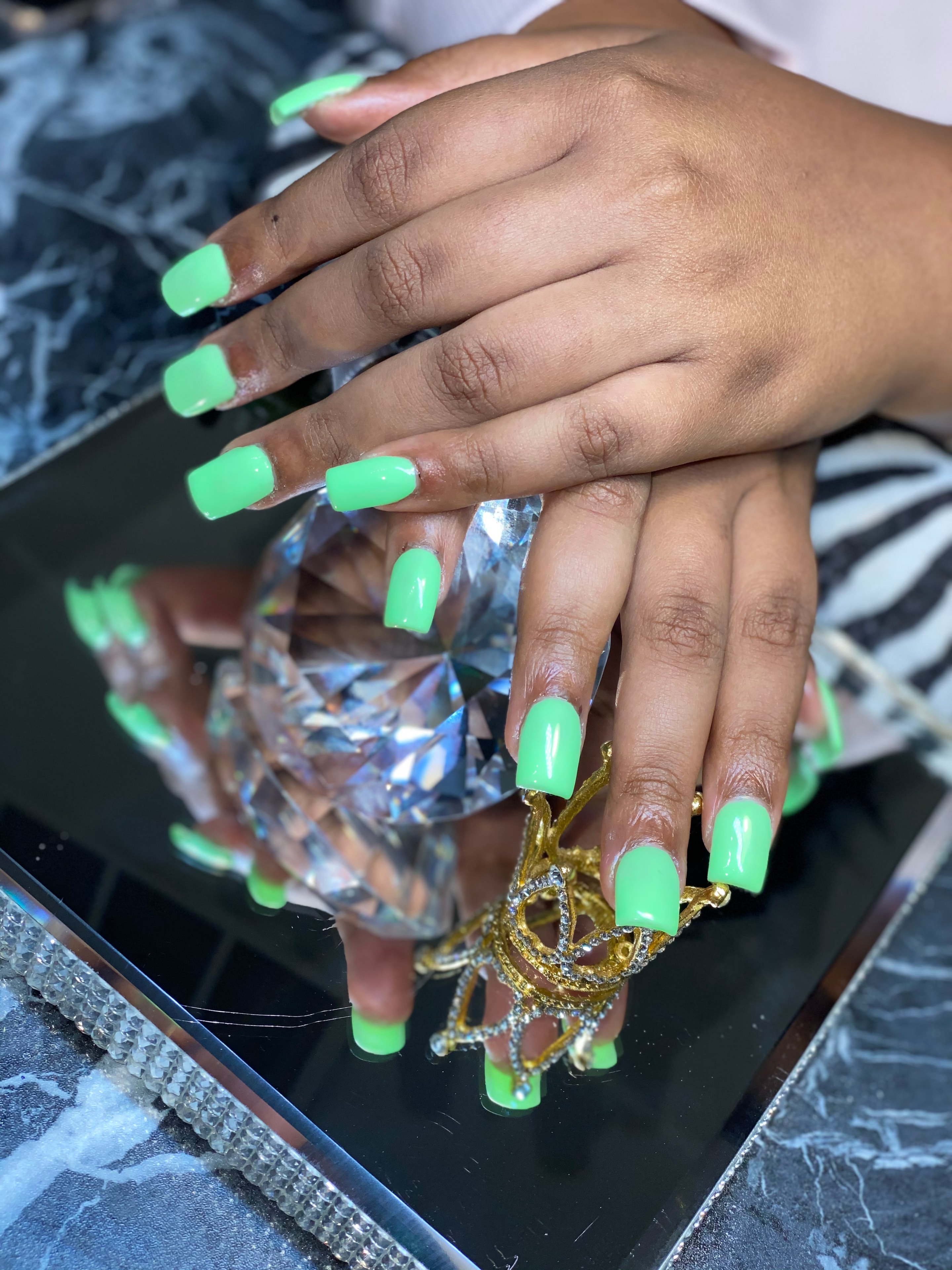 Neon green acrylic nailz posed on a mirrored tray with a jeweled crown
