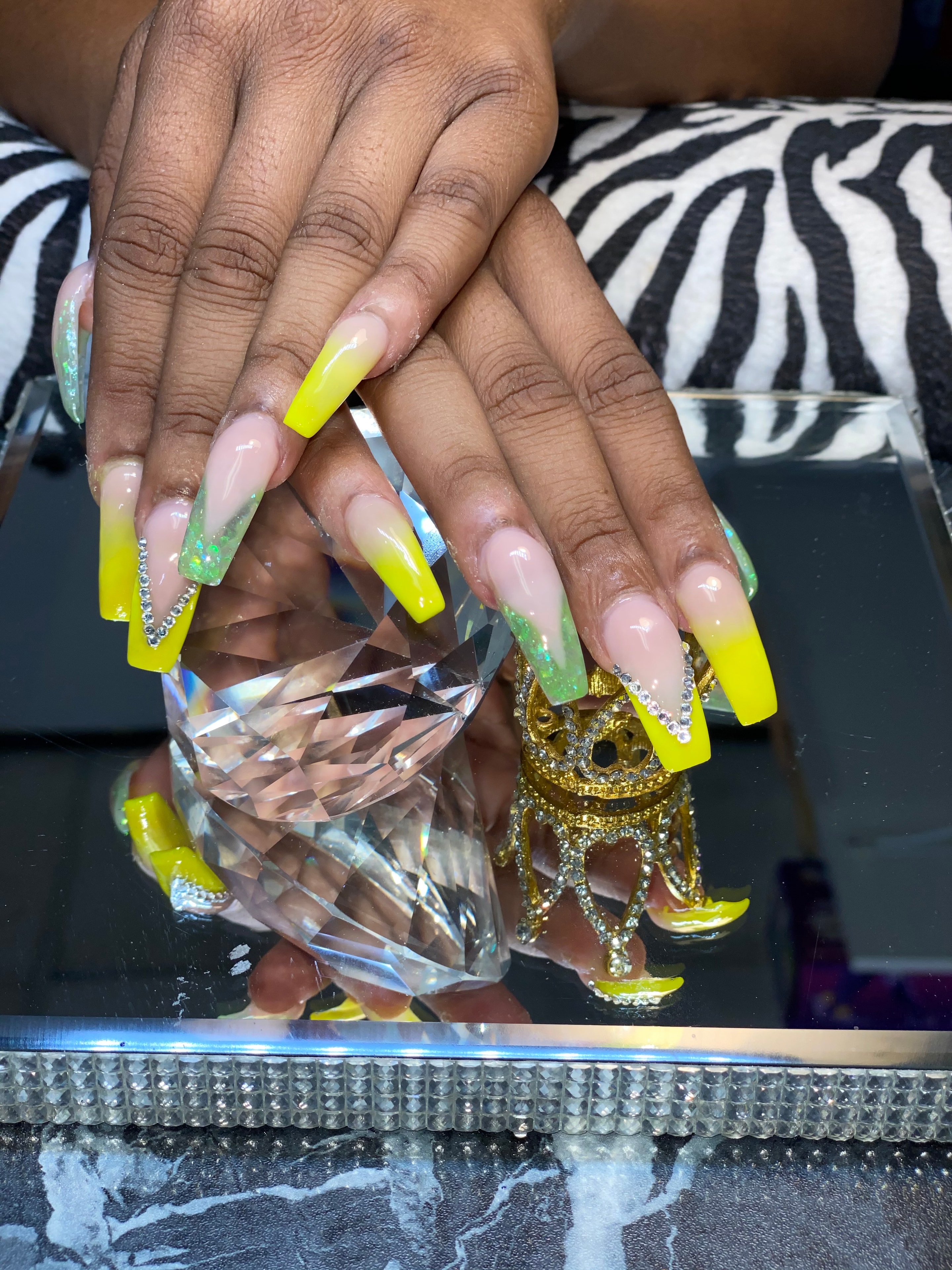 Long coffin nailz with neon yellow French tips, green glitter accents, and rhinestones held over a crystal